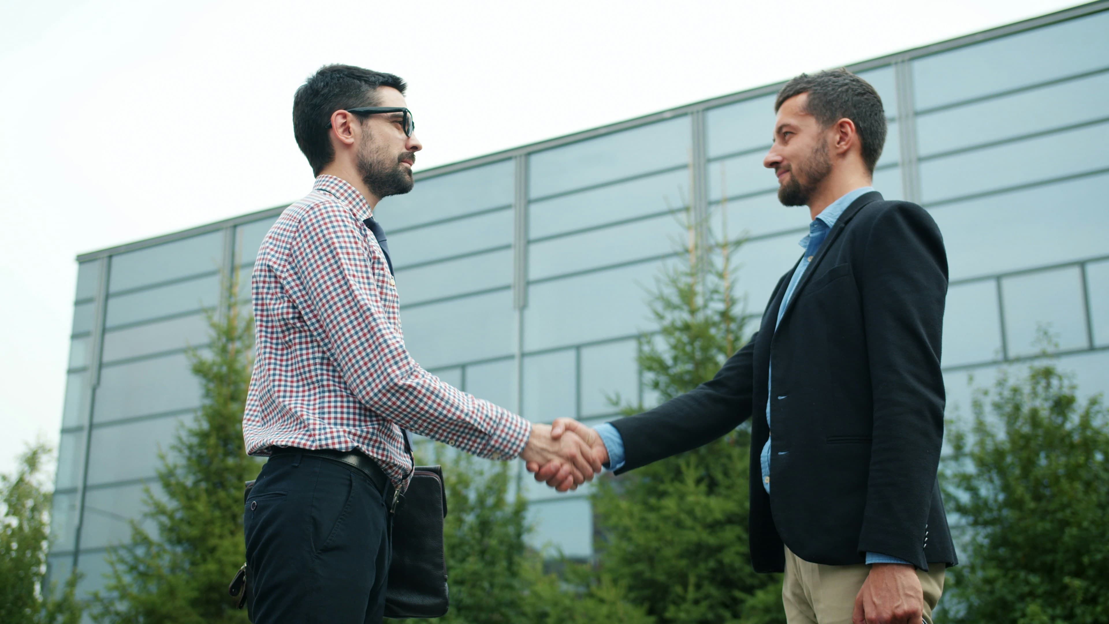 Dois empresários apertando as mãos em frente a um prédio moderno